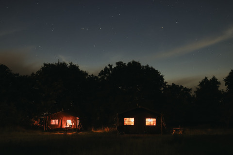 Foto nocturna de cabañas iluminadas en Feather Down Les Jardins des Coccinelles, parque vacacional en Bretaña, Francia.