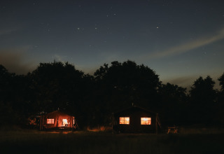 Foto nocturna de cabañas iluminadas en Feather Down Les Jardins des Coccinelles, parque vacacional en Bretaña, Francia.