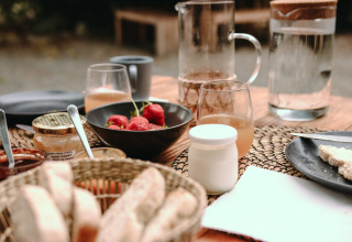 Desayuno en Feather Down Les Jardins des Coccinelles con pan, fresas, miel y bebidas refrescantes.