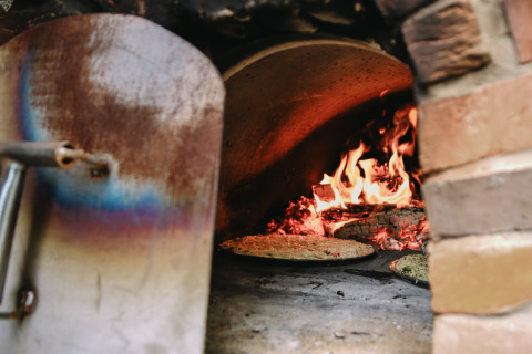Ein holzbefeuerter Pizzaofen mit brennendem Feuer, der Pizza bäckt, im Les Jardins des Coccinelles.