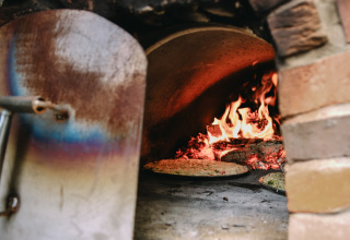 Ein holzbefeuerter Pizzaofen mit brennendem Feuer, der Pizza bäckt, im Les Jardins des Coccinelles.