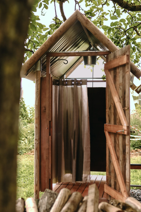 Douche extérieure dans une cabane en bois rustique à Feather Down Les Jardins des Coccinelles, Bretagne, France.