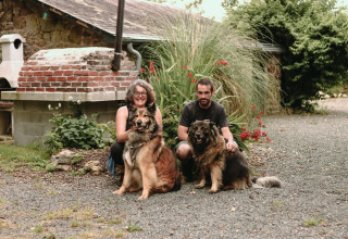 A couple kneels outdoors with two large dogs in a garden at Feather Down Les Jardins des Coccinelles, Brittany.