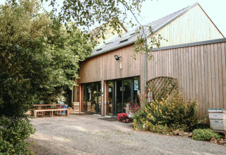 Et træbeklædt feriehus med store vinduer og have ved Feather Down Les Jardins des Coccinelles i Bretagne, Frankrig.