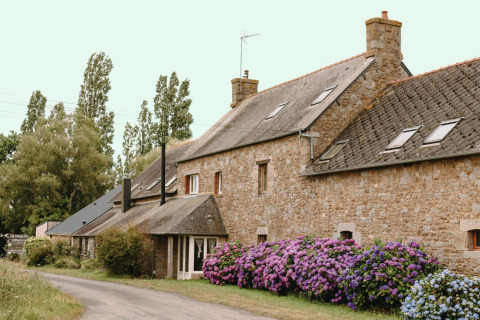 Casa de piedra con hortensias en flor y árboles altos en Les Jardins des Coccinelles, Bretaña, Francia.