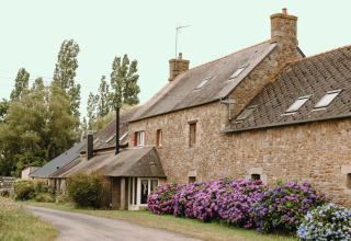 Casa in pietra circondata da ortensie fiorite e alberi a Les Jardins des Coccinelles in Bretagna, Francia.