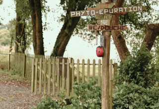 Houten wegwijzer in Feather Down Les Jardins des Coccinelles vakantiepark in Bretagne, Frankrijk, tussen het groen.