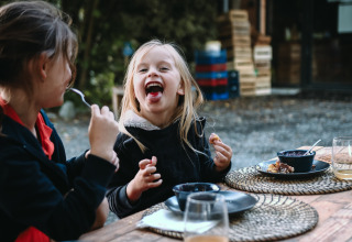 Twee kinderen genieten van een maaltijd buiten bij Feather Down Les Jardins des Coccinelles in Bretagne, Frankrijk.