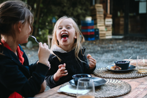Zwei Kinder essen gemeinsam draußen in Feather Down Les Jardins des Coccinelles in der Bretagne, Frankreich.