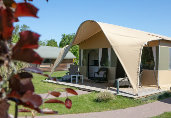 Luksusteltet Lodge ved Holiday Park 't Rheezerwold i Holland med terrasse og havemøbler på en solrig dag.
