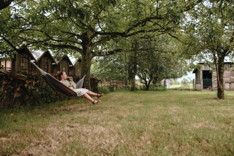 Woman relaxing in a hammock under trees at Feather Down Les Jardins des Coccinelles holiday park in Brittany.