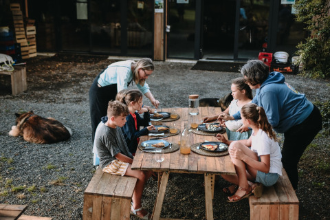 Familia comiendo al aire libre en una mesa de madera en Feather Down Les Jardins des Coccinelles, Bretaña, Francia.