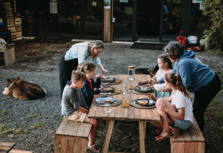 Famiglia che cena all'aperto a un tavolo di legno a Feather Down Les Jardins des Coccinelles in Bretagna.