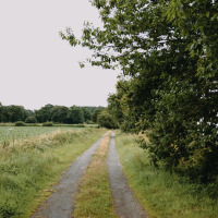 Camino rural entre campos verdes y árboles cerca de Val-Couesnon, Bretaña, Francia, bajo un cielo nublado.