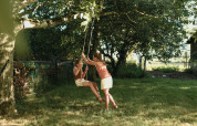 Twee kinderen spelen op een schommel onder een boom bij Feather Down Les Jardins des Coccinelles, Bretagne, Frankrijk.