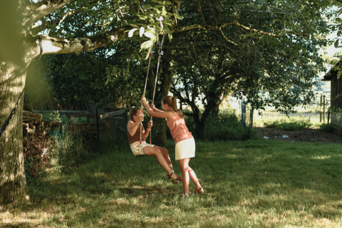 Zwei Kinder spielen auf einer Schaukel unter Bäumen bei Feather Down Les Jardins des Coccinelles, Bretagne, Frankreich.