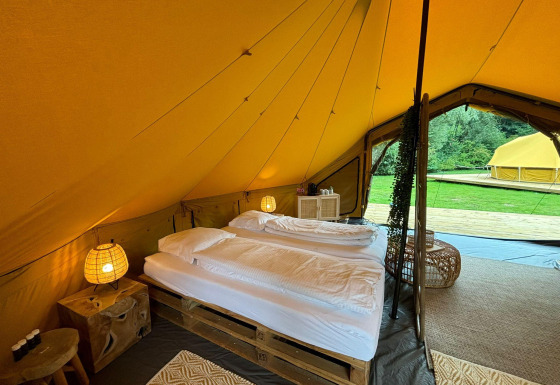 Vista interna di una tenda safari di lusso con letto matrimoniale e arredi accoglienti a Urban-Gardens, Belgio.