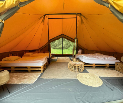 Interno di una tenda safari di lusso con due letti matrimoniali su pallet e arredo naturale in Belgio.