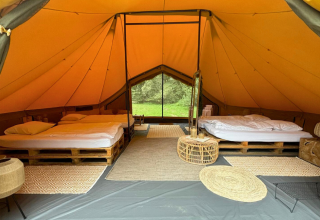Interieur van een luxe safaritent met twee bedden op pallets en gezellige, natuurlijke aankleding in België.