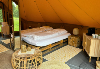 Interieur van safaritent Bivak Deluxe - Gent bij Urban-Gardens, België, met tweepersoonsbed en rieten meubels.