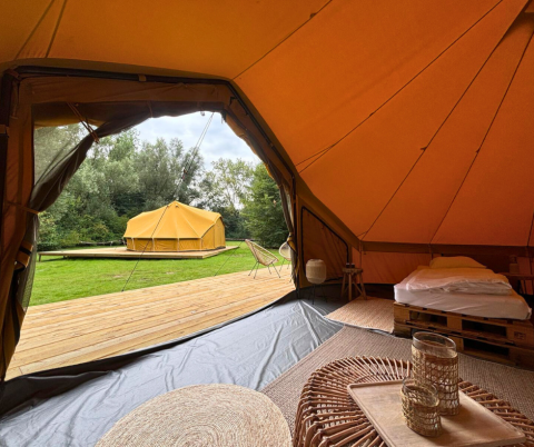 Binnenaanzicht van een safaritent met comfortabele inrichting, houten vlonder en andere tent bij Urban-Gardens Gent.