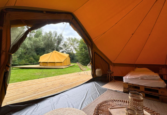 Interior view from a safari tent showing cozy furnishings, wooden decking, and another tent at Urban-Gardens Gent.