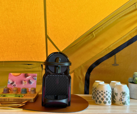 Cafetera, tazas y cápsulas en mesa dentro de tienda safari en Bivak Deluxe - Gent, Urban-Gardens, Bélgica.