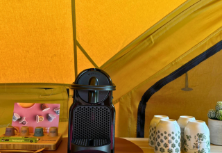 Cafetera, tazas y cápsulas en mesa dentro de tienda safari en Bivak Deluxe - Gent, Urban-Gardens, Bélgica.