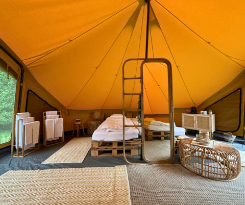 Interior acogedor de tienda safari con cama doble, espejo grande y decoración natural en Bélgica.