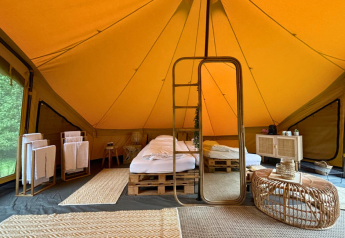 Cozy safari tent interior with a double bed, floor rugs, a large mirror, and rustic decor in Belgium.