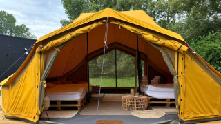 Tienda safari Bivak Deluxe - Gent con dos camas, terraza de madera y entorno natural verde vistos desde fuera.