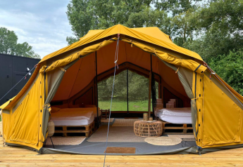 Tienda safari Bivak Deluxe - Gent con dos camas, terraza de madera y entorno natural verde vistos desde fuera.