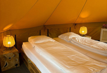 Interior of Bivak Deluxe - Gent safari tent at Urban-Gardens, Belgium with twin beds, lamps, and cozy decor.