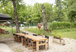 Buiten eetgedeelte met houten tafel en stoelen bij Camping Pittoresque in het groene Occitanie, Frankrijk.