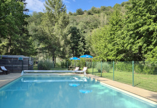 Piscina all’aperto circondata da alberi e colline verdi al Camping Pittoresque in Occitania, Francia.