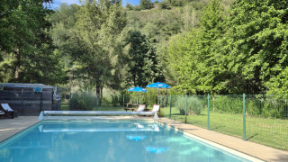 Piscina al aire libre rodeada de árboles y colinas en Camping Pittoresque en Occitania, Francia.