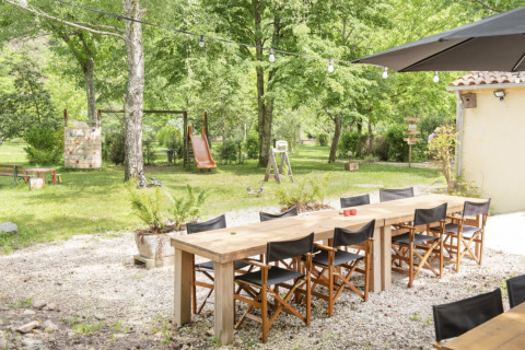 Zona de comedor al aire libre en Camping Pittoresque, Occitanie, Francia, con mesas, sillas y un parque infantil.