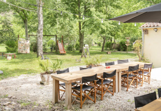 Zona de comedor al aire libre en Camping Pittoresque, Occitanie, Francia, con mesas, sillas y un parque infantil.
