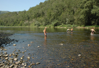 Camping Pittoresque in Occitanie, Frankrijk, met mensen die pootjebaden in een ondiepe rivier bij het bos.