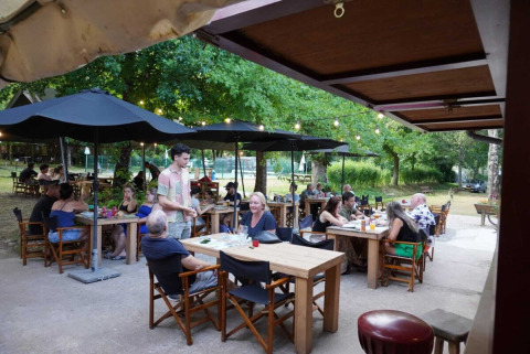 Persone che cenano all'aperto sotto ombrelloni neri al Camping Pittoresque in Occitania, Francia.