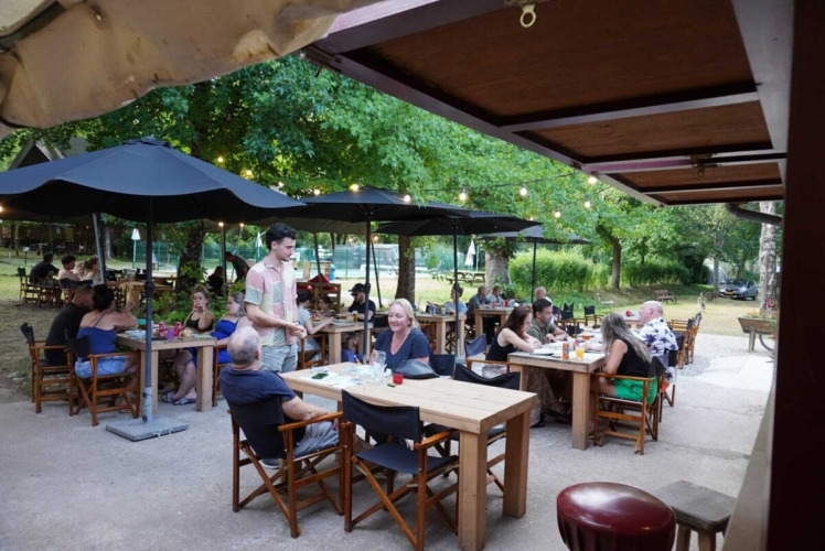 People dining outdoors under black umbrellas at Camping Pittoresque holiday park in Occitanie, France.