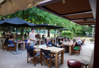 People dining outdoors under black umbrellas at Camping Pittoresque holiday park in Occitanie, France.