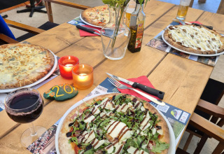 Bord med pizzaer, vin, stearinlys og blomster på Camping Pittoresque i Occitanie, Frankrig.