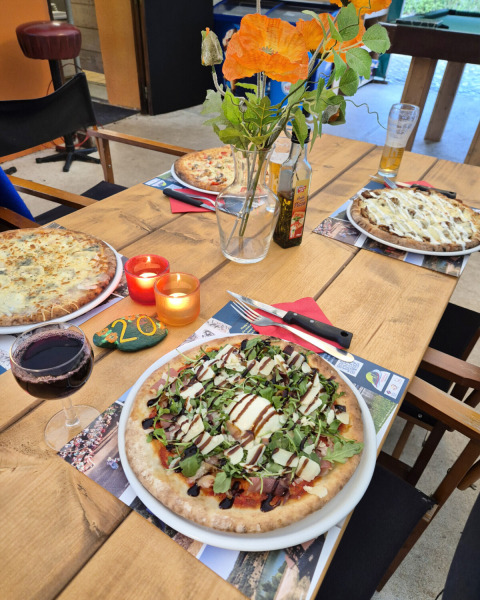 Tisch mit Pizzen, Wein, Kerzen und Blumen bei Camping Pittoresque in Occitanie, Frankreich.