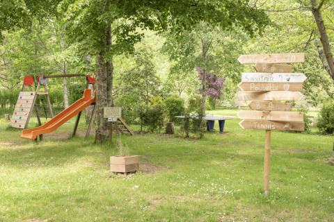 Parque infantil y letreros de madera en Camping Pittoresque, un parque vacacional en Occitania, Francia.