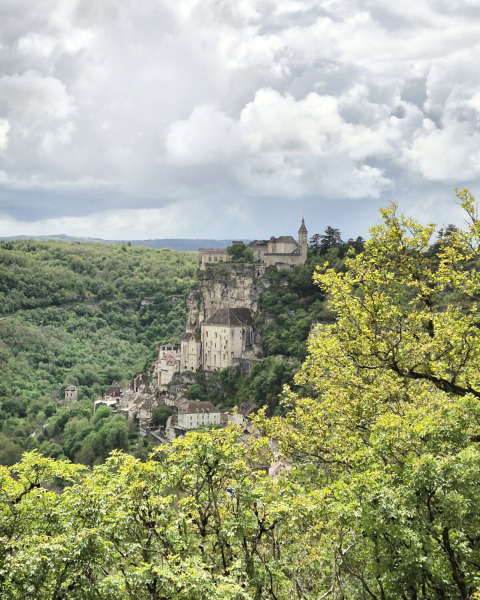 Scenic view of a cliffside village with historic buildings and lush trees at Camping Pittoresque, Occitanie, France.