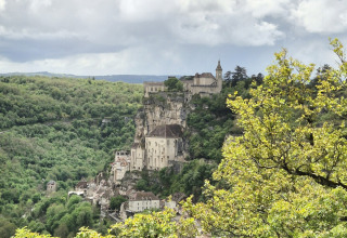 Blick auf eine mittelalterliche Klippenstadt mit üppigen Bäumen bei Camping Pittoresque in Occitanie, Frankreich.