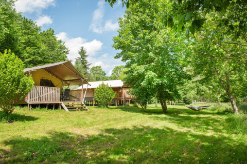 Teltlodges og grønne træer ved Camping Pittoresque, et feriepark i Occitanie, Frankrig, under en blå himmel.