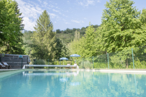 Piscina exterior en Camping Pittoresque, un parque vacacional en Occitania, Francia, rodeada de árboles verdes.