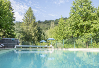 Piscina all'aperto al Camping Pittoresque in Occitania, Francia, circondata da alberi verdi e natura.